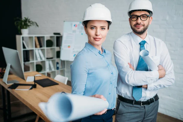 Smiling architects standing at modern office with building plans — Stock Photo