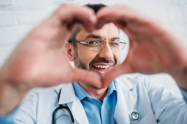 Feliz médico guapo mostrando el signo del corazón con las manos — Stock Photo