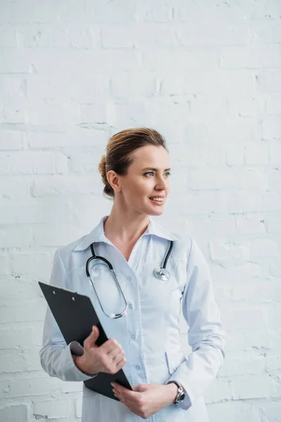 Attraente medico femminile con appunti davanti al muro di mattoni bianchi — Foto stock