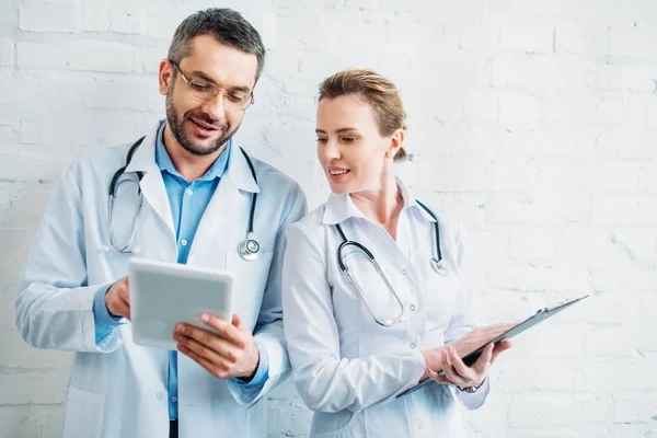 Zufriedene Ärzte arbeiten mit Tablet und Klemmbrett zusammen — Stockfoto