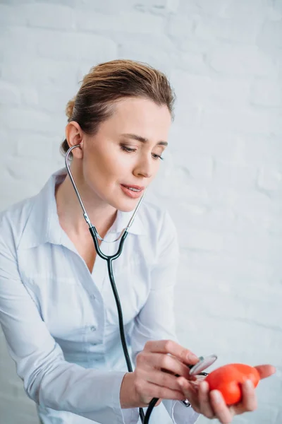 Female doctor listening heartbeat of toy heart with stethoscopes — Stock Photo