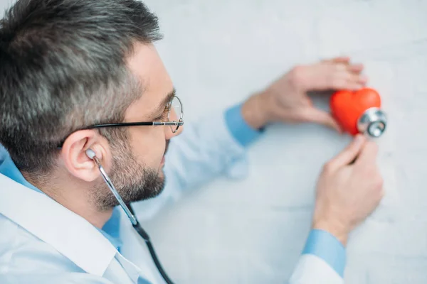 Männlicher Arzt hört Herzschlag von Spielzeugherz mit Stethoskopen — Stockfoto