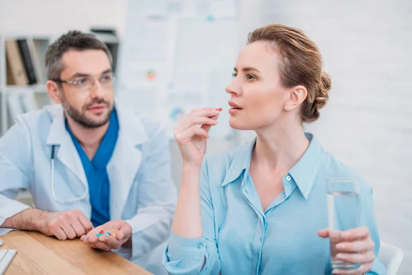 Mujer de negocios tomando píldora mientras que el médico dando consulta - foto de stock