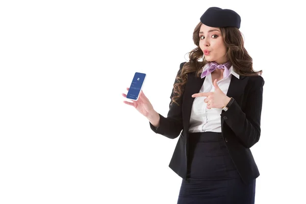 Schöne Stewardess zeigt auf Smartphone mit Facebook-Website isoliert auf weiß — Stockfoto