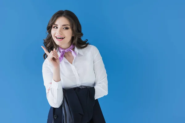 Lächelnde schöne Stewardess, die einen Finger isoliert auf blau zeigt — Stockfoto