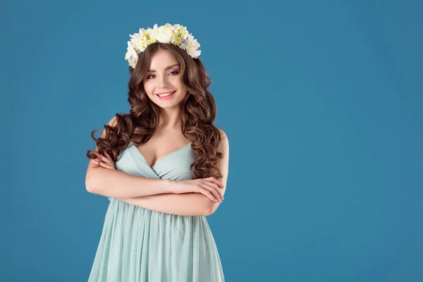 Menina bonita com flores grinalda na cabeça de pé com braços cruzados isolados em azul — Fotografia de Stock