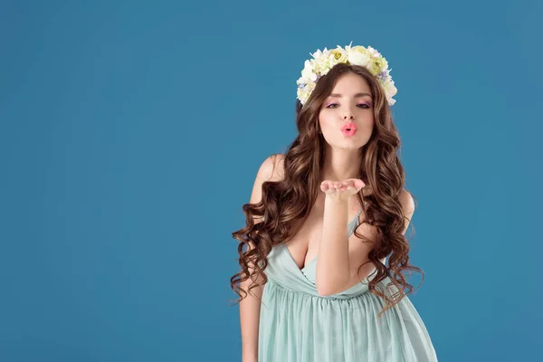 Beautiful girl with flowers wreath on head sending air kiss isolated on blue — Stock Photo