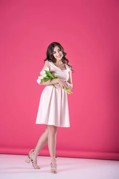 Attractive girl in pink dress with bouquet of tulips looking away on pink — Stock Photo
