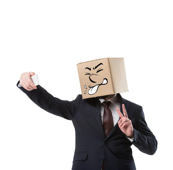 Businessman with cardboard box on head taking selfie on smartphone isolated on white — Stock Photo