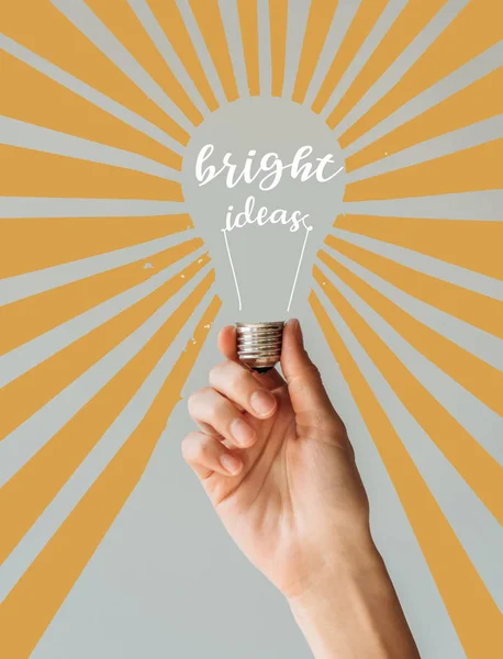 Cropped image of woman holding light bulb with inscription bright ideas and orange rays isolated on gray — Stock Photo