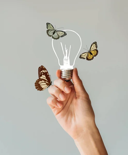 Abgeschnittenes Bild einer Frau, die eine Lampe mit Schmetterlingen in der Hand hält, isoliert auf grau — Stockfoto
