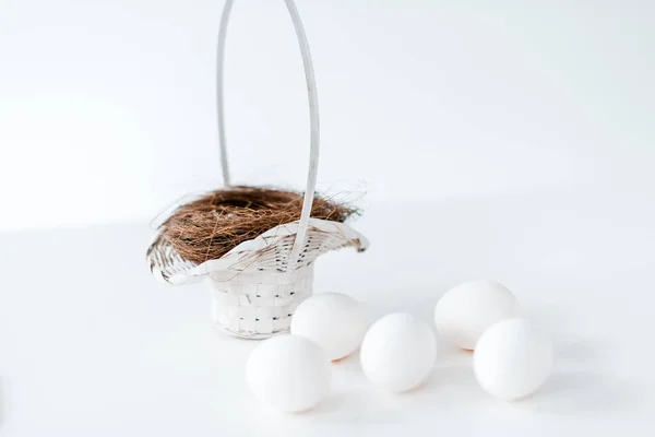 Nahaufnahme von weißen Hühnereiern und Nest im Weidenkorb auf weiß — Stockfoto