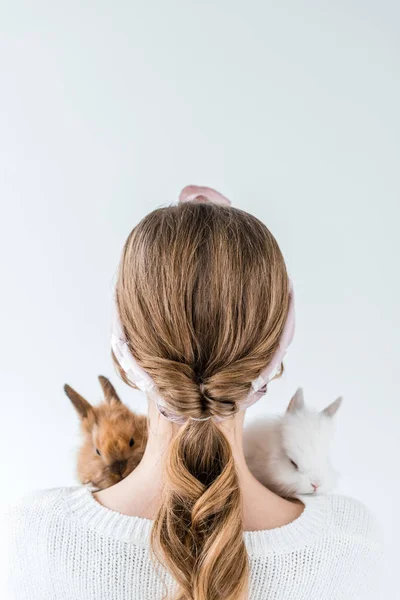 Vista trasera de niña sosteniendo adorables conejos peludos aislados en blanco - foto de stock