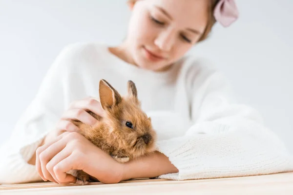 Vista de cerca de la chica sonriente sosteniendo adorable conejo peludo en blanco - foto de stock