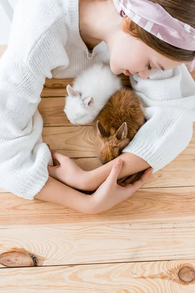 Vista superior de la niña abrazando lindos conejos peludos en la mesa de madera - foto de stock