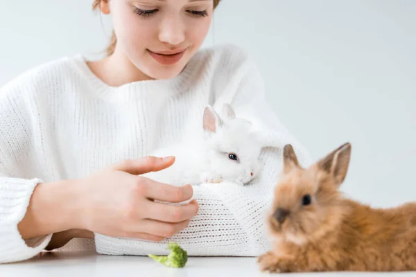 Recortado tiro de sonriente chica alimentación conejos con brócoli en blanco - foto de stock