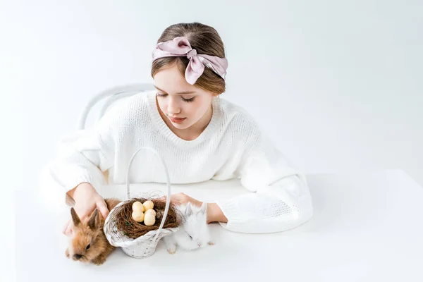 Linda menina olhando para coelho e cesta com ovos de Páscoa no ninho — Fotografia de Stock
