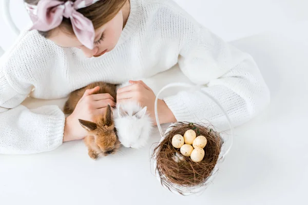 Plan recadré de fille regardant mignons lapins à fourrure et panier avec des œufs de Pâques dans le nid — Photo de stock