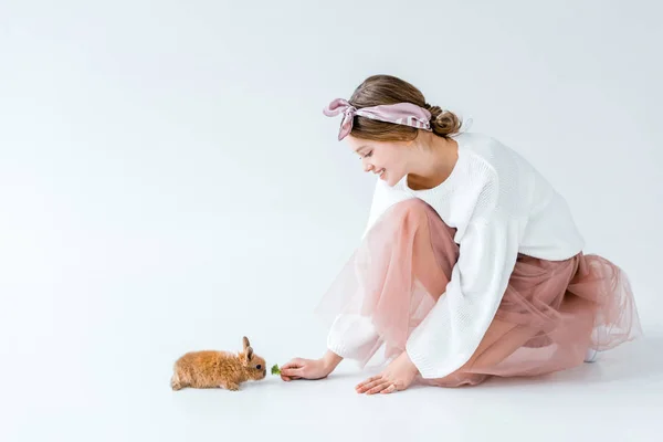 Side view of beautiful smiling girl feeding furry rabbit isolated on white — Stock Photo