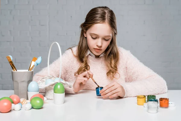 Hermosa niña pintando huevos de Pascua en la mesa - foto de stock