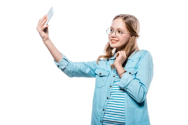 Hermosa adolescente feliz en gafas tomando selfie con teléfono inteligente aislado en blanco - foto de stock