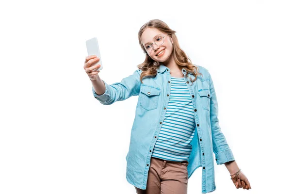 Linda chica adolescente sonriente en gafas tomando selfie con teléfono inteligente aislado en blanco - foto de stock