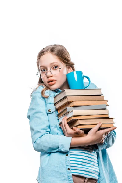 Menina em óculos segurando pilha de livros com copo em cima e olhando para a câmera isolada no branco — Fotografia de Stock