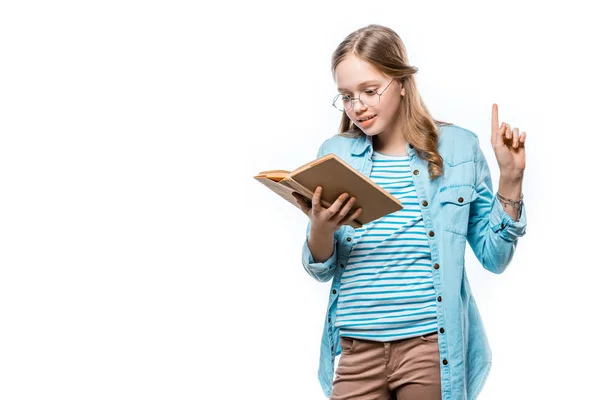 Hermosa adolescente en gafas lectura libro y apuntando hacia arriba con el dedo aislado en blanco - foto de stock