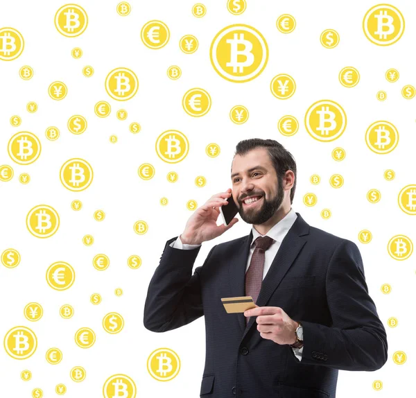 Hombre de negocios con tarjeta de crédito hablando en el teléfono inteligente, bitcoin y símbolos de dinero aislados en blanco - foto de stock