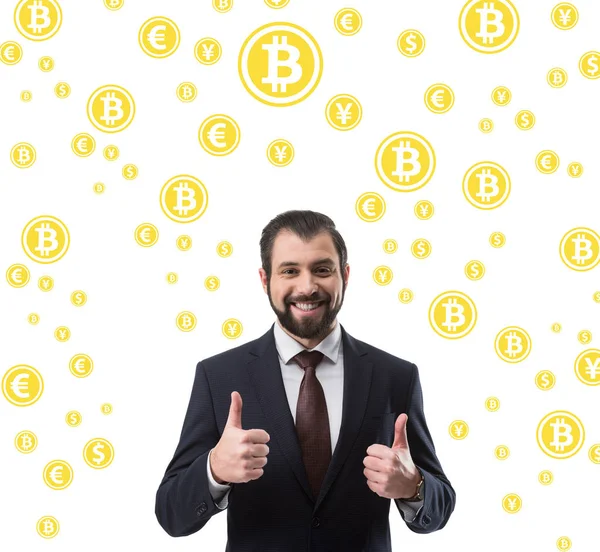 Barbudo sonriente hombre de negocios en traje que muestra los pulgares hacia arriba, bitcoin y símbolos de dinero aislados en blanco - foto de stock