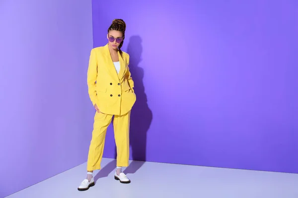 African american girl posing in trendy yellow suit and purple sunglasses, on ultra violet background — Stock Photo