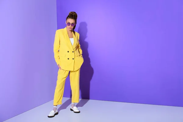 Afro-américaine fille posant en costume jaune à la mode et lunettes de soleil violettes, sur fond ultraviolet — Photo de stock