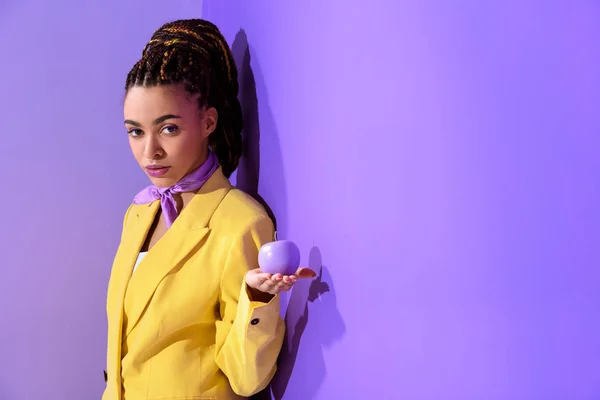 African american girl posing in yellow suit with purple apple, on trendy ultra violet background — Stock Photo