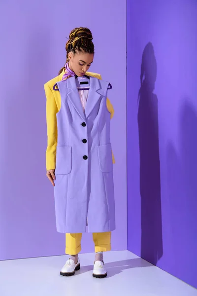 Elegant african american girl in yellow suit holding purple waistcoat, on trendy ultra violet background — Stock Photo