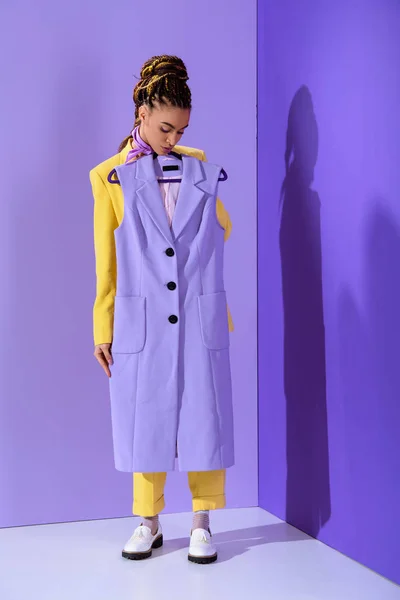 Elegante chica afroamericana en traje amarillo sosteniendo chaleco púrpura, sobre fondo ultra violeta de moda - foto de stock