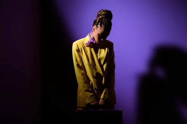 Menina americana africana elegante posando em terno amarelo no escuro, na moda fundo ultravioleta — Fotografia de Stock