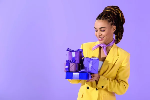 Afro-américaine en costume jaune tenant des cadeaux violets, sur fond ultra violet à la mode — Photo de stock