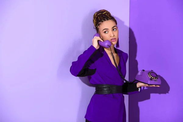 Модная мулатка разговаривает по ротационному телефону на ультрафиолетовой стене — стоковое фото