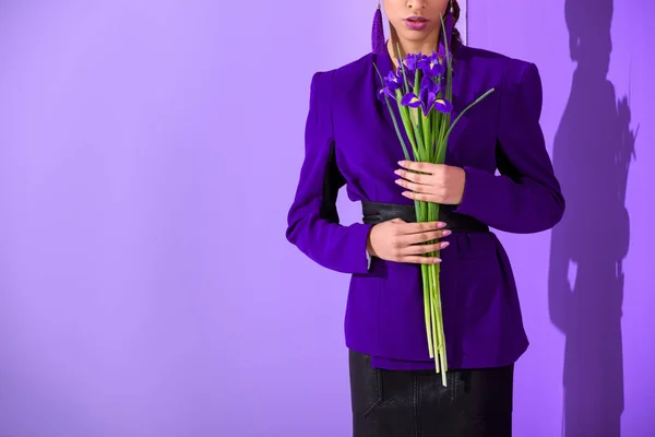 Cropped view of mulatto girl posing in purple jacket with irises at ultra violet wall — Stock Photo