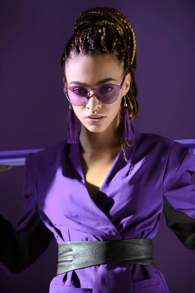 Stylisches Mulattin posiert in ultravioletter Jacke und Sonnenbrille, isoliert auf lila — Stockfoto
