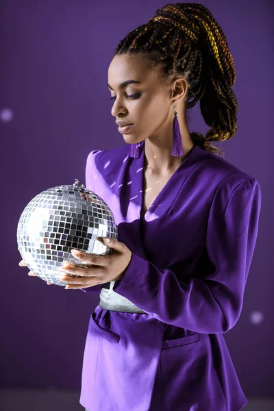 Menina americana africana bonita em casaco roxo olhando para bola de discoteca, isolado em roxo — Fotografia de Stock