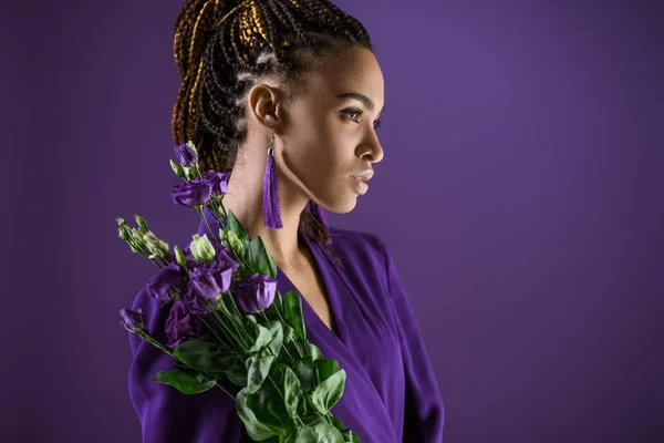 Fille afro-américaine à la mode posant avec des fleurs d'eustomes violettes, isolée sur violet, tendance ultra violette — Photo de stock