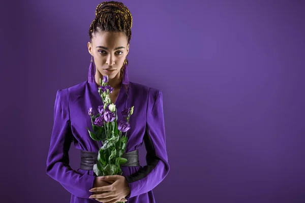Modèle mulâtre élégant posant avec des fleurs violettes, isolé sur ultraviolet — Photo de stock