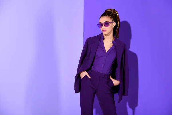 Chica afroamericana elegante posando en traje púrpura y gafas de sol, tendencia ultra violeta - foto de stock