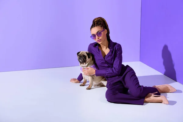 Elegante mulatto ragazza in posa in abito viola alla moda con cane carlino, tendenza ultra viola — Foto stock