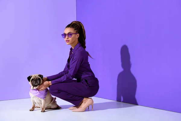 Attrayant afro-américain jeune femme posant en costume violet avec carlin, tendance ultra violet — Photo de stock