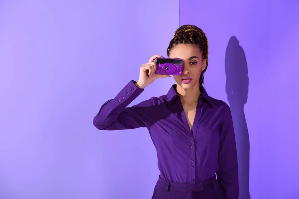 Stylish beautiful mulatto girl in purple jacket taking photo on camera — Stock Photo