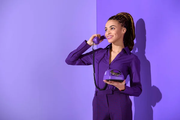 Attractive mulatto girl talking on rotary phone at ultra violet wall — Stock Photo
