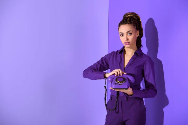 Модная африканская американка держит ретро-телефон у ультрафиолетовой стены — стоковое фото