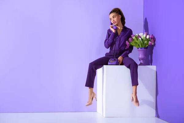Mode belle fille mulâtre parler sur téléphone rotatif et assis sur cube avec des tulipes — Photo de stock